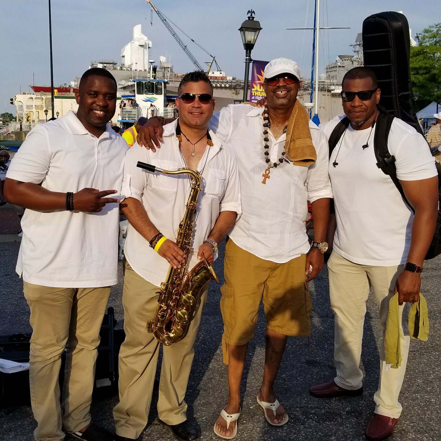four men wearing white polo shirts and khaki pants with one holding a saxophone