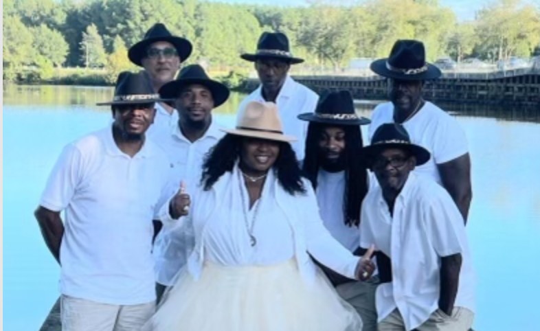 Band members dressed in white with black hats. Femail lead singer in tan hat.