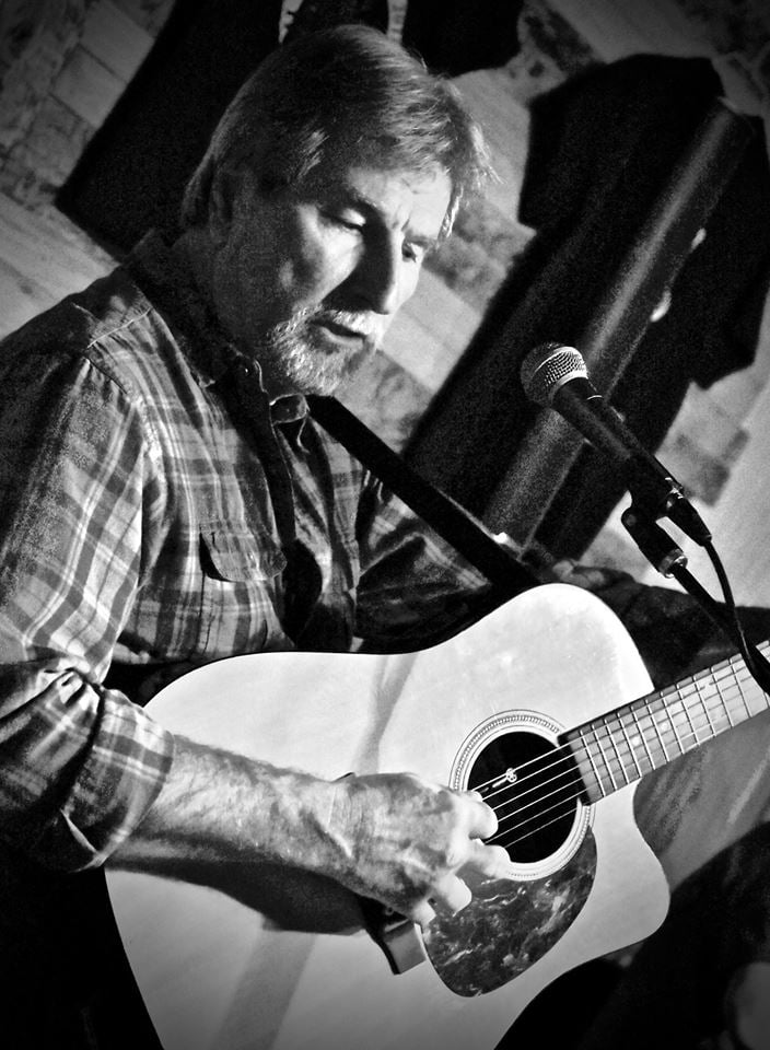 Jim Masters playing guitar wearing a plaid shirt