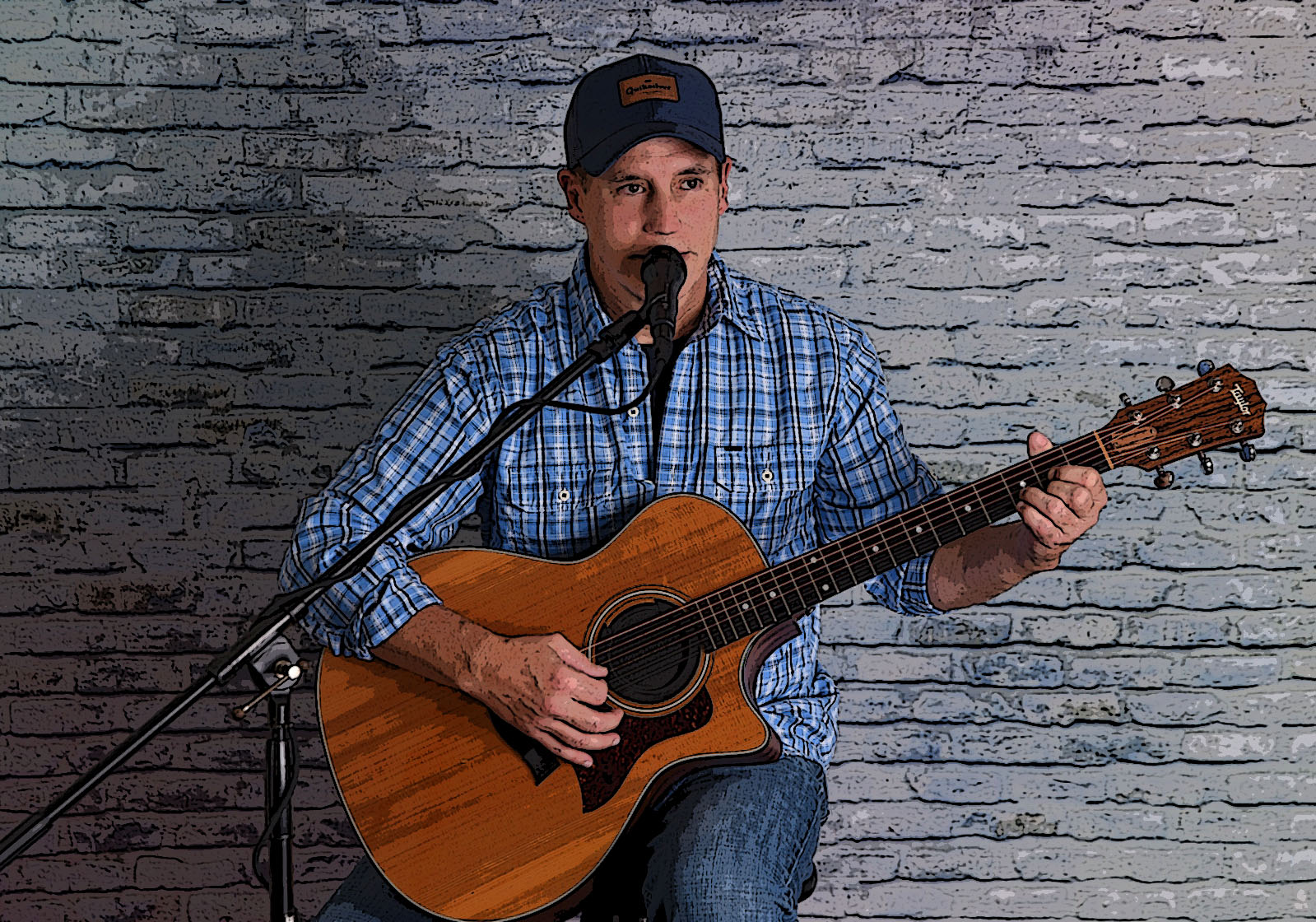 Man in blue paid shirt playing guitar and singing with brick wall background