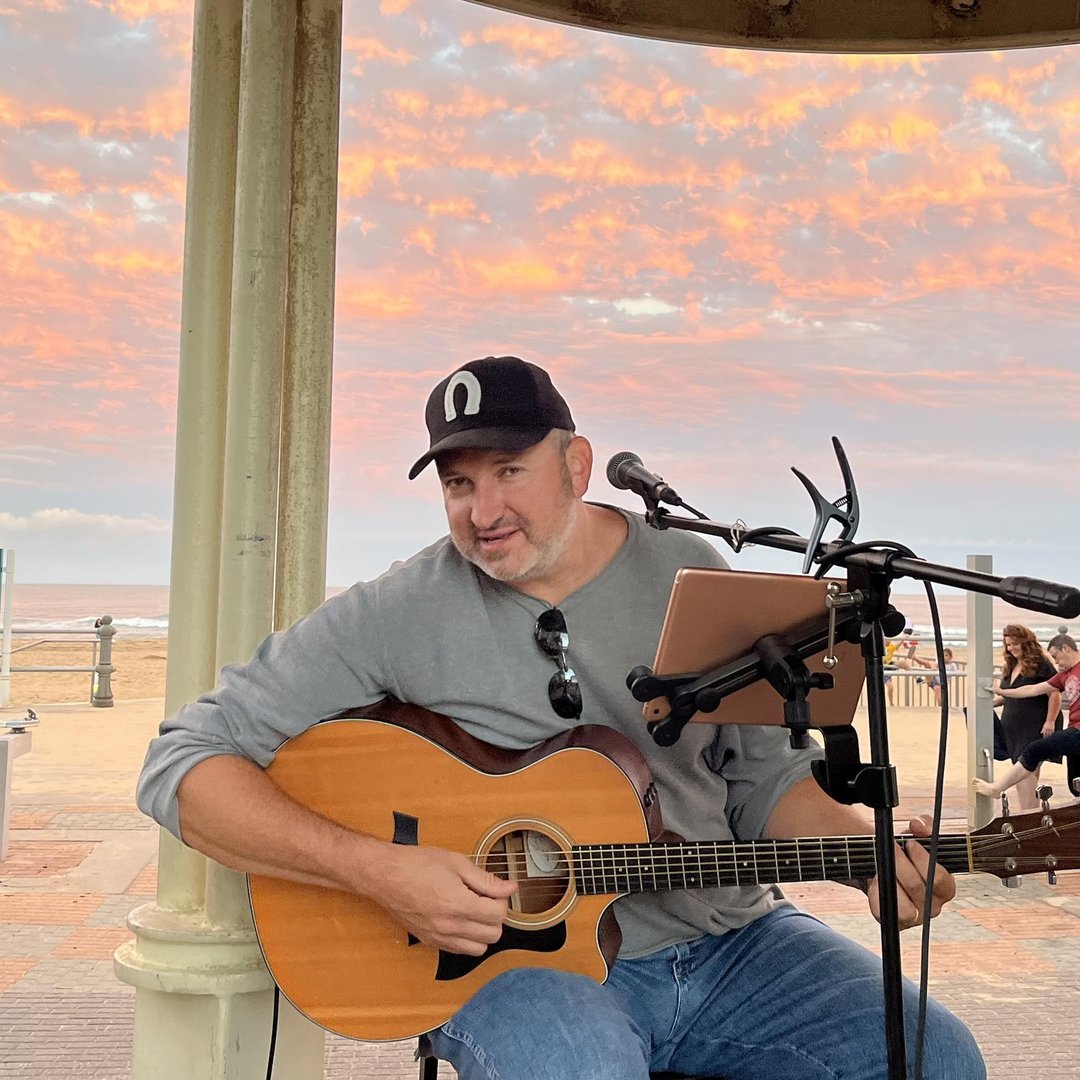 Brian Pinardi playing guitar with a sunset sky behind him