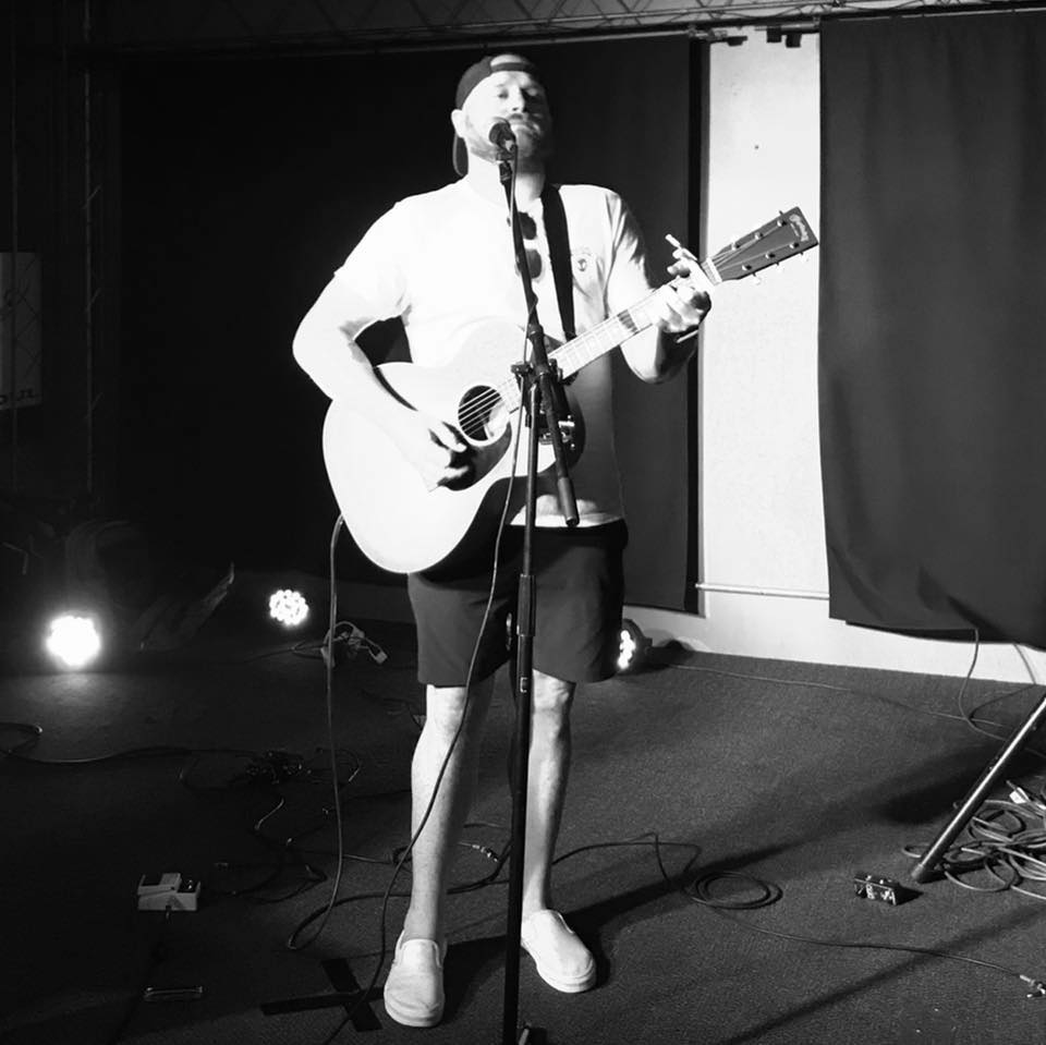 Seth Logan playing guitar and singing wearing shorts and a t shirt