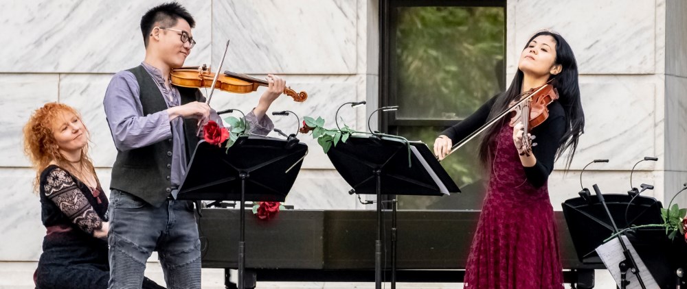 three musicians, two playing violin and one playing piano