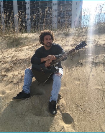 Kerry Bess sitting on sand dune with guitar