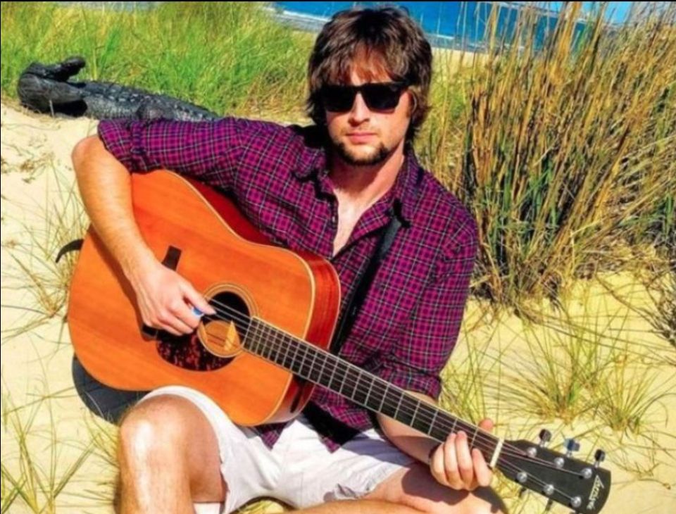 Marty Moore with guitar on a beach